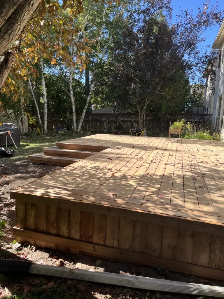 A Stittsville wood deck taking in the sunshine partially under the shade of a tree in the backyard